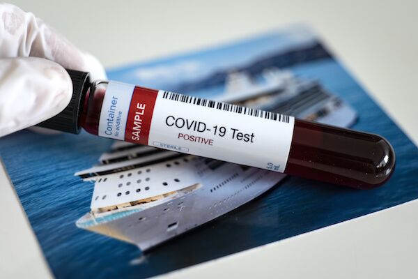 A gloved hand hold a vial labeled “COVID-19 Test” above a photograph of a cruise ship.